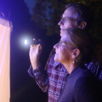Two moth night event attendees looking for moths on collection sheet.