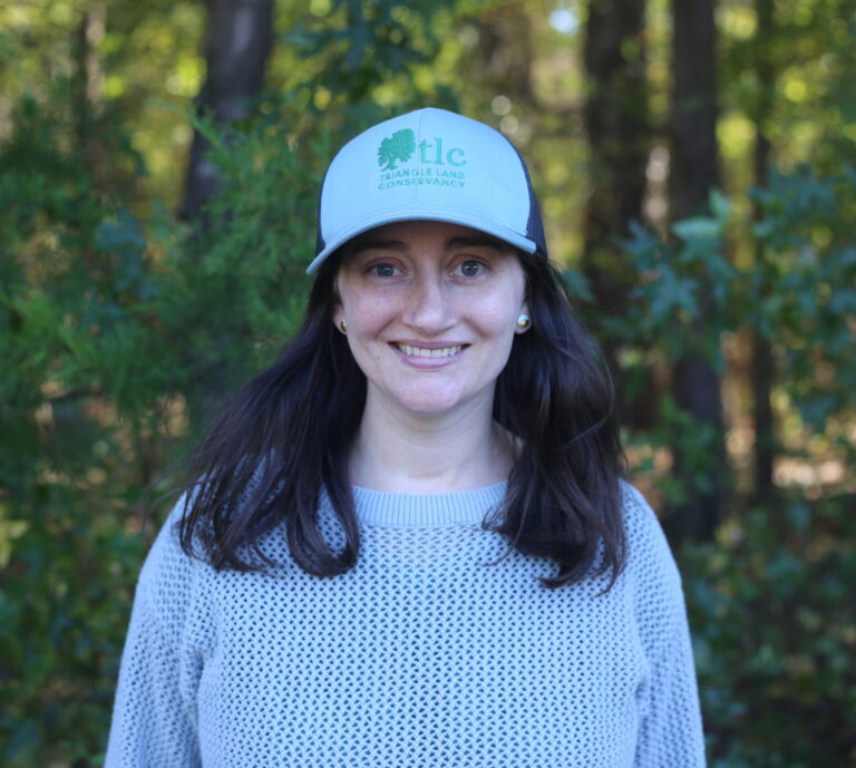 Brenna Thompson smiling in front of a dense forest background.