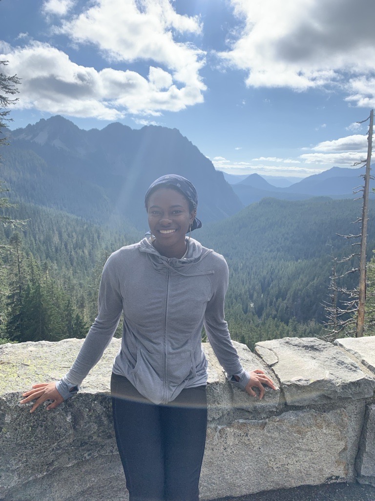 Kierra Hyman standing on a stony scenic overlook with large forested mountains in the background.