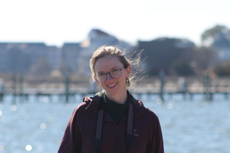 Kayla Ebert smiling outside a blurred out water landscape.